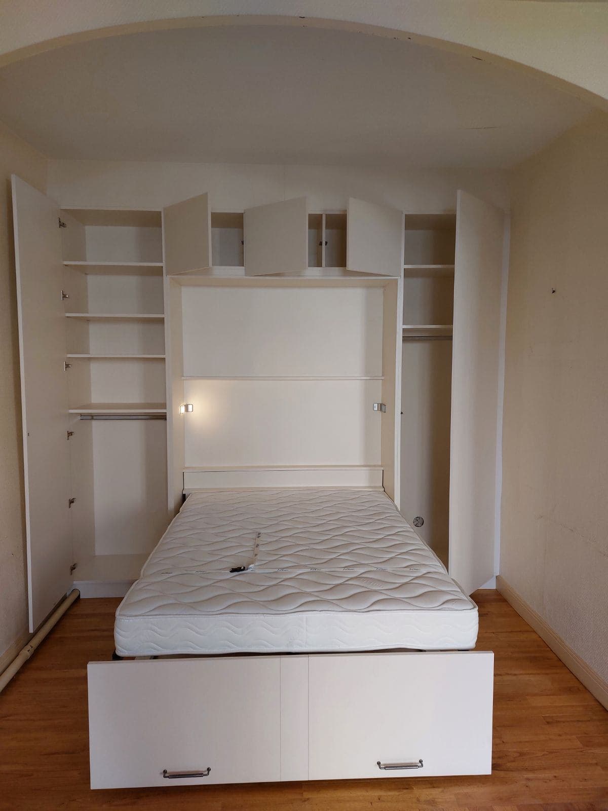 Lit escamotable 140 cm déplié, dressings latéraux ouverts à étagères et penderies, coffre bas blanc