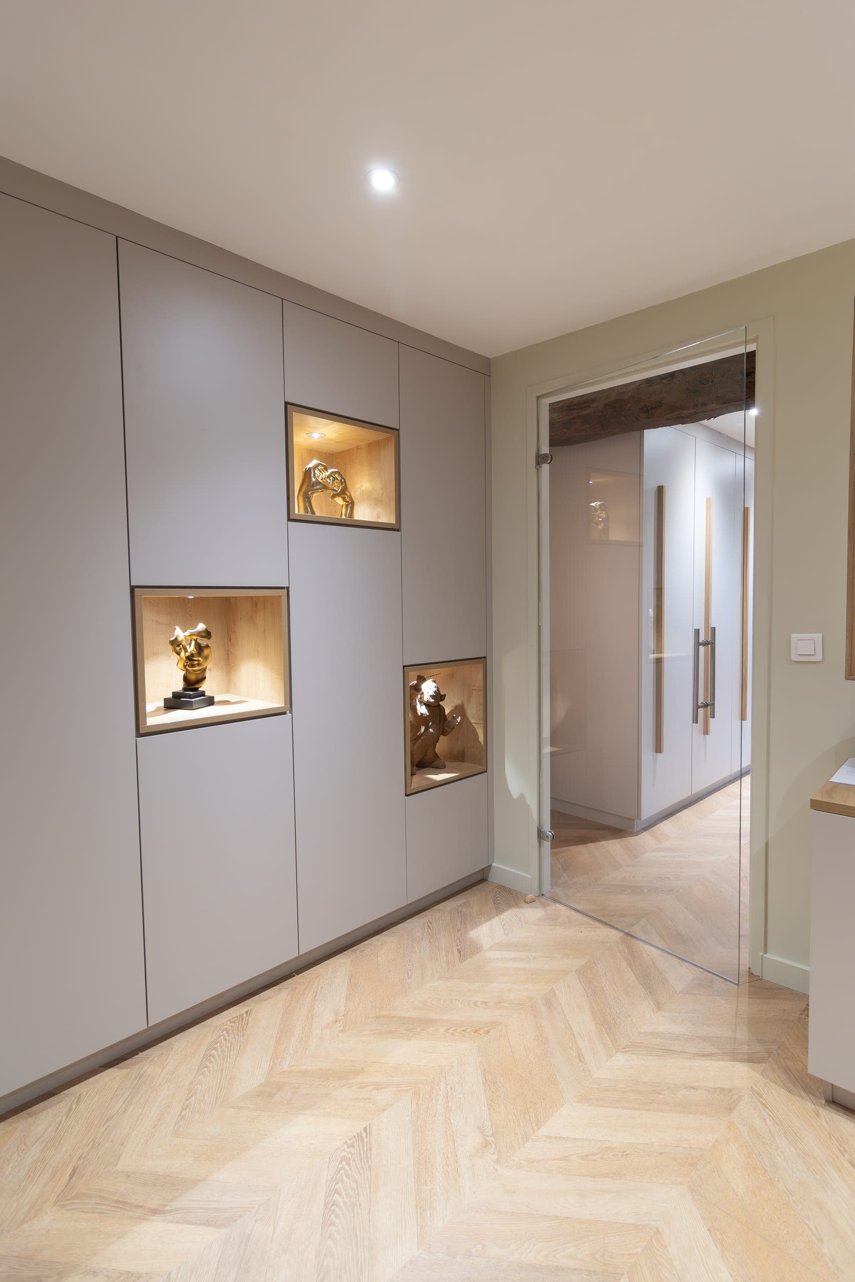 Dressing à portes cachemire avec niches éclairées présentant des sculptures dorées, ouverture vitrée sur couloir