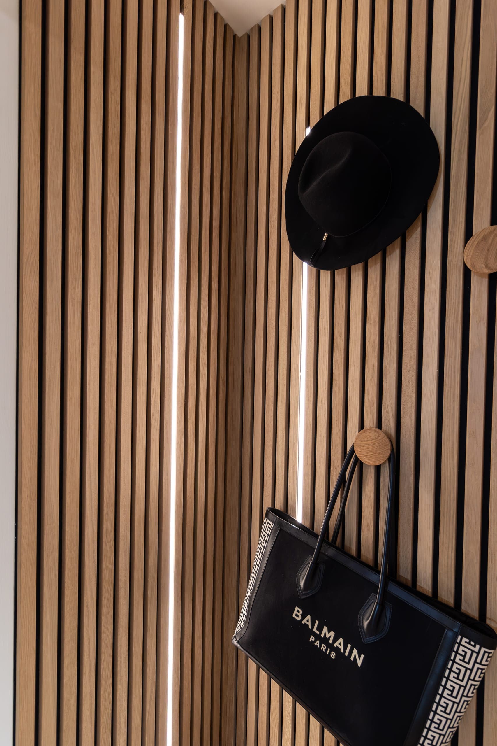 Gros plan d’un claustra de tasseaux bois avec ruban led, patères et chapeau accroché