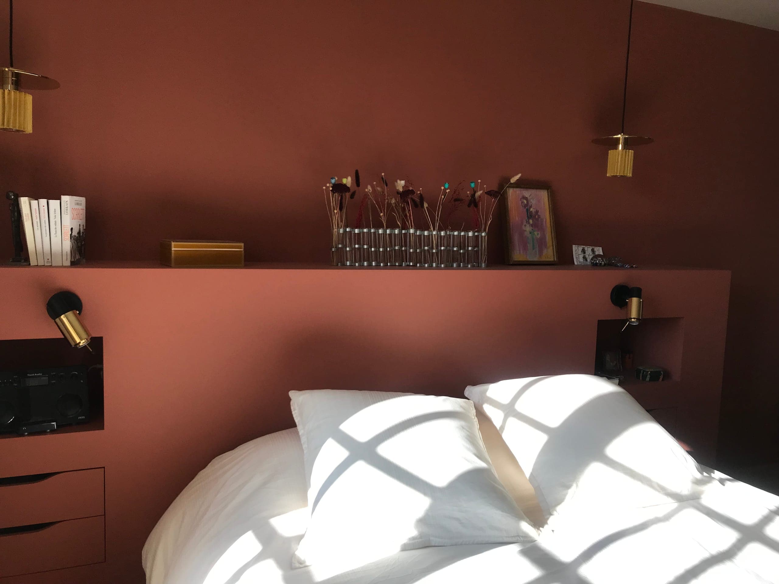 Détail de la tête de lit terracotta : niche avec liseuse laiton, tablette garnie de livres et fleurs séchées