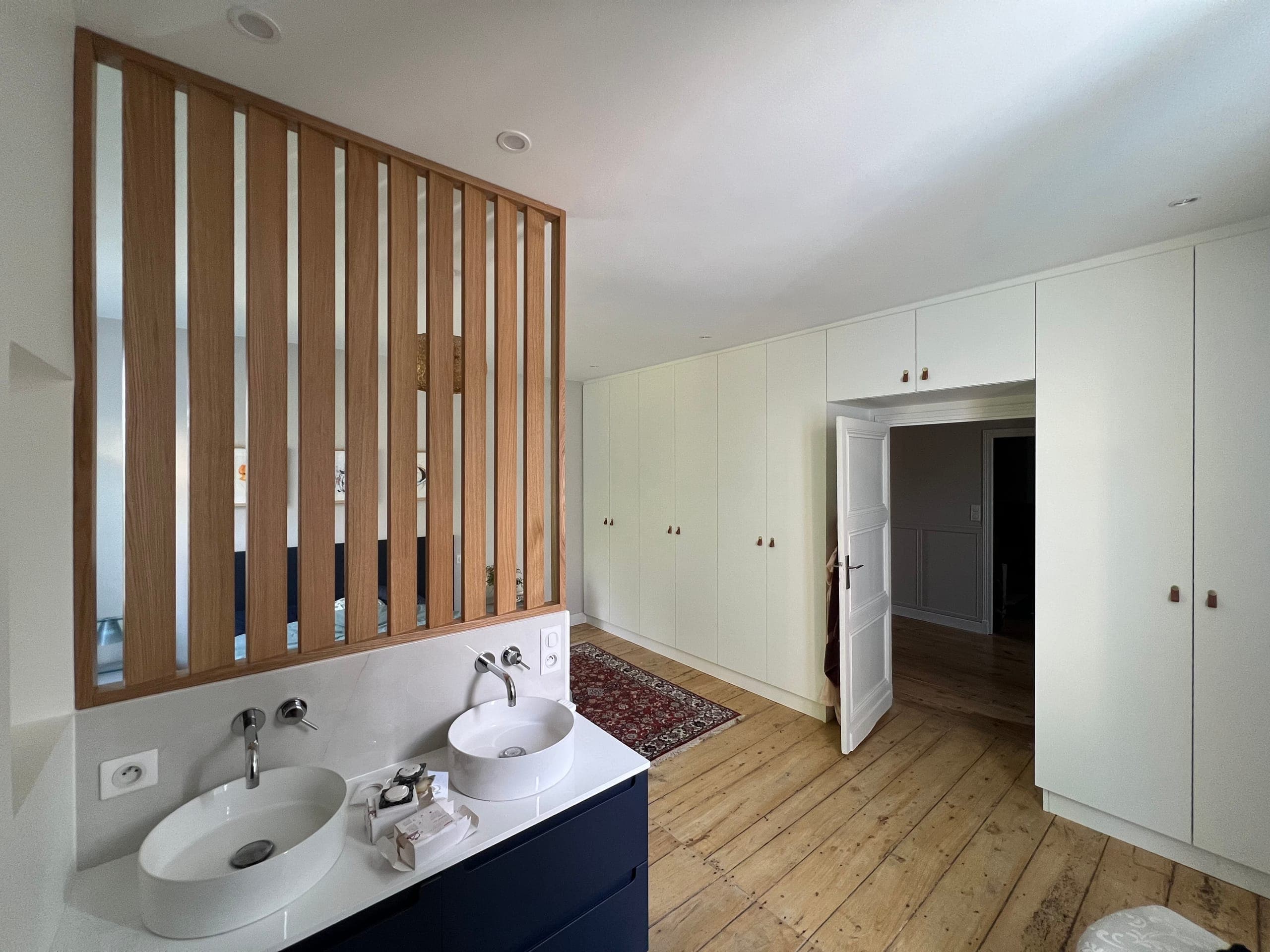 Claustra en chêne à lames verticales au-dessus du meuble double vasque bleu nuit, séparant la salle de bain du dressing
