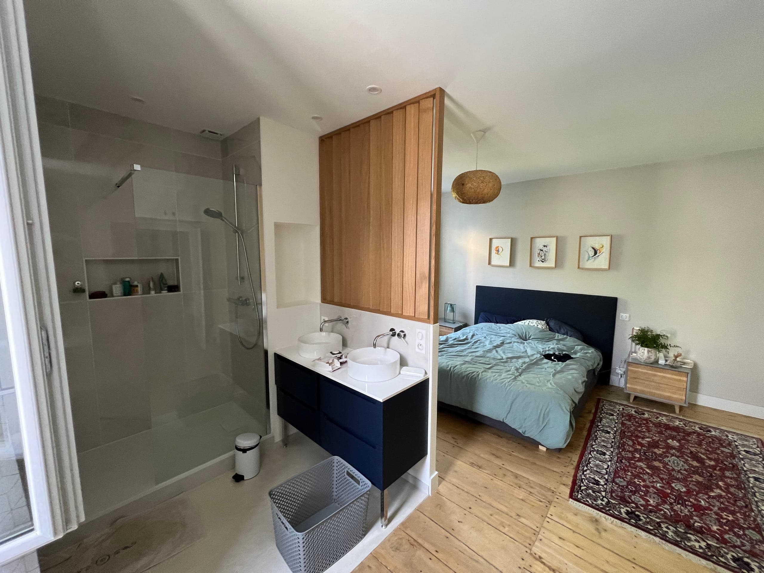 Suite parentale avec douche à l’italienne, meuble double vasque bleu nuit et claustra bois séparant l’espace bain de la chambre