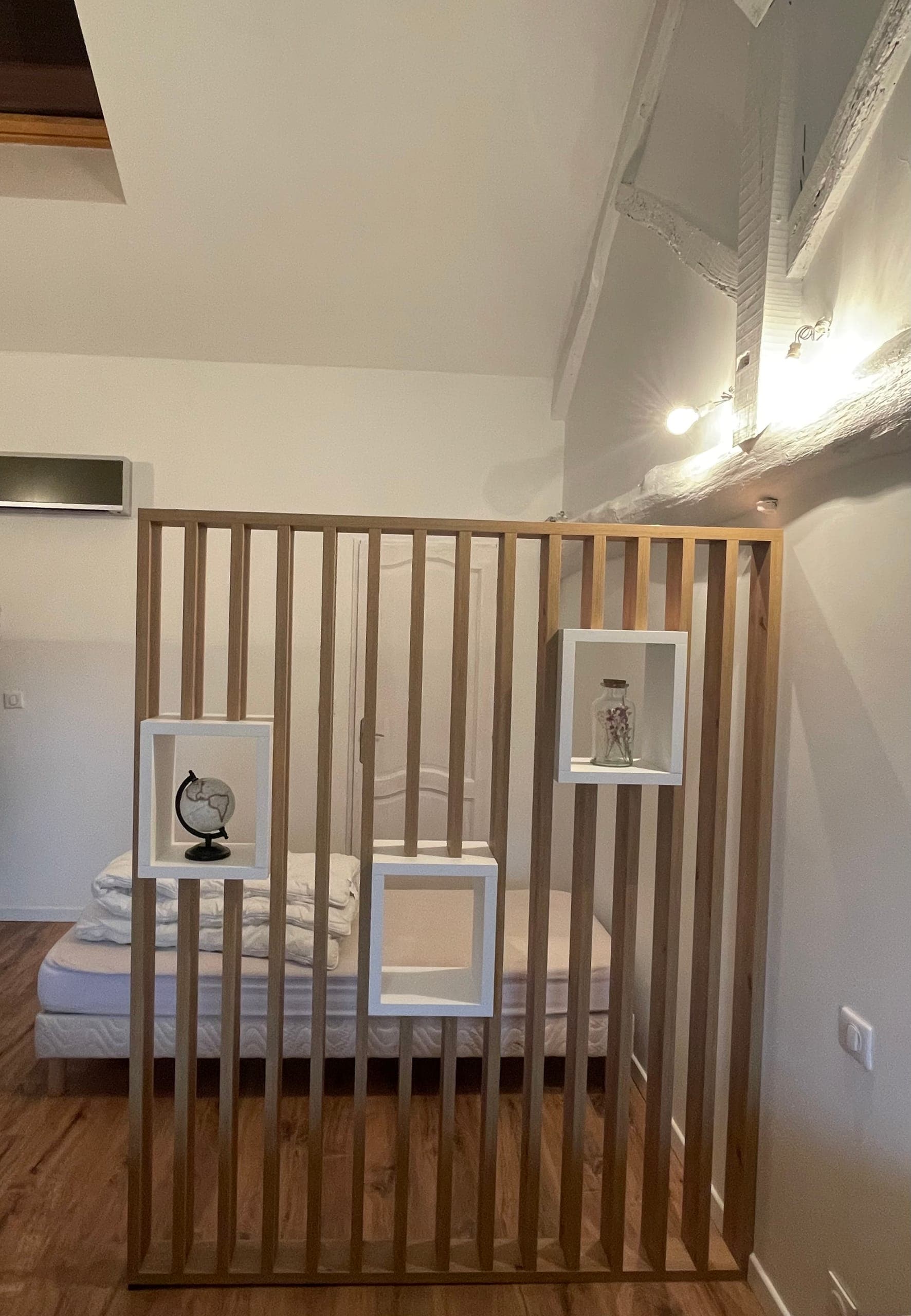 Claustra toute hauteur en chêne huilé avec trois niches blanches séparant deux espaces dans une chambre