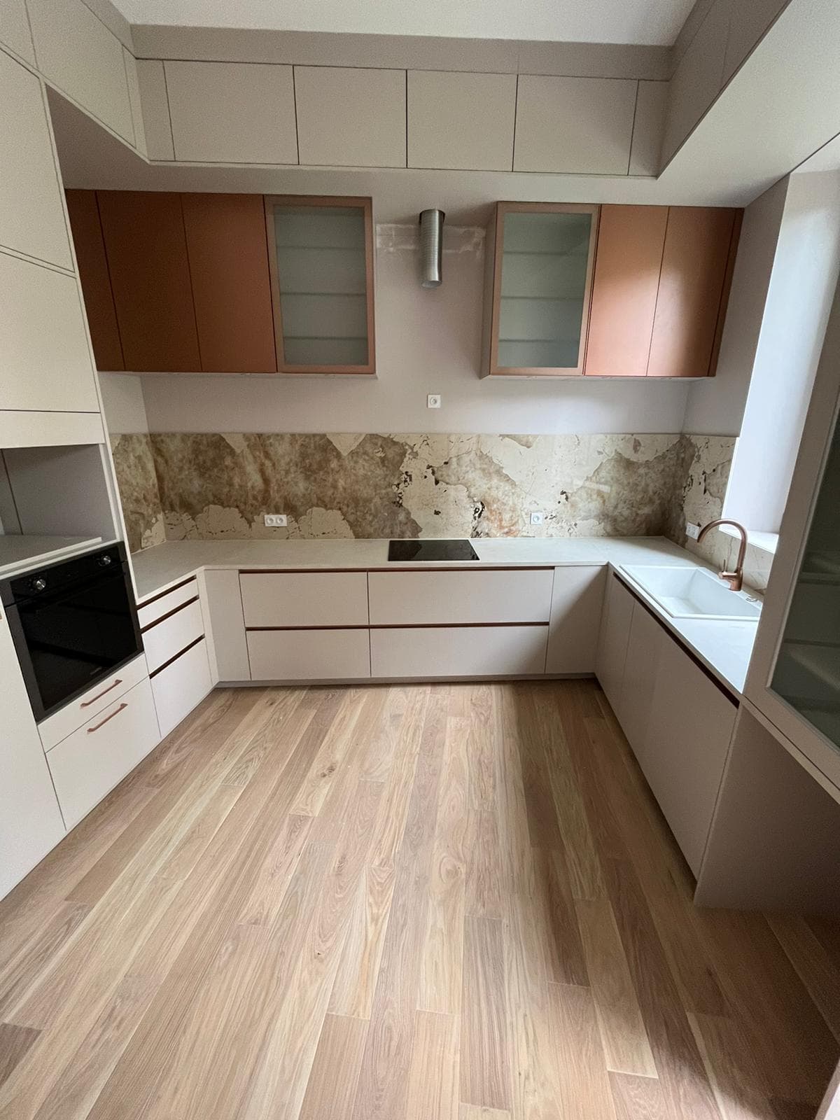 Vue d’ensemble en U, meubles hauts cuivrés et vitrés, hotte murale, parquet chêne clair
