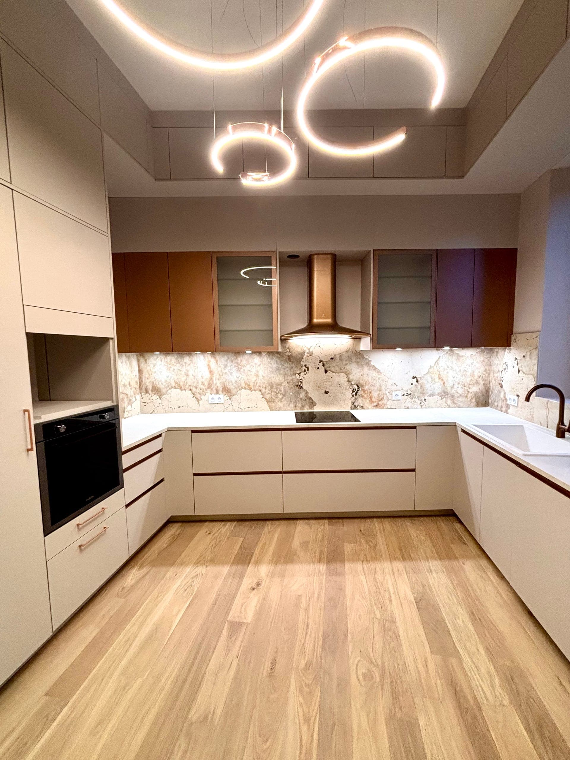 Cuisine en U éclairée, suspensions lumineuses circulaires, hotte cuivrée et crédence dekton veiné