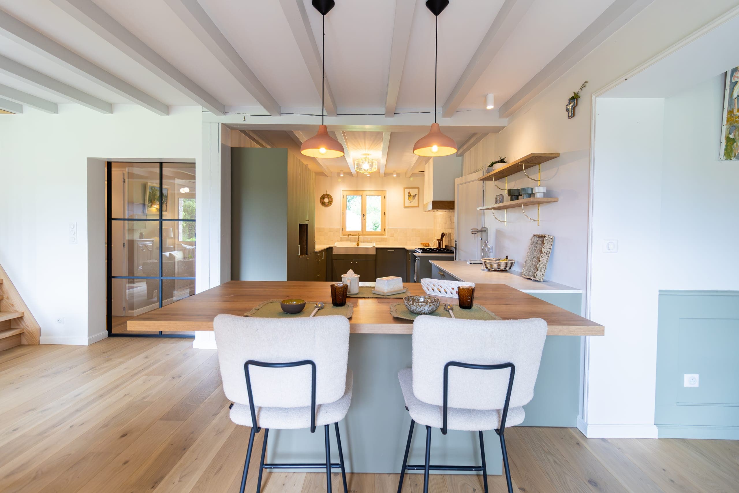 Îlot central en bois avec deux tabourets bouclette blanche, verrière noire et plafond à poutres claires