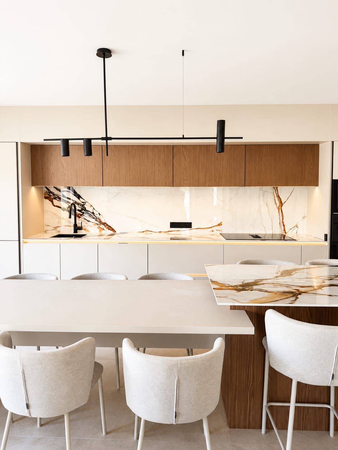Cuisine du pavillon vue de face : meubles hauts en bois, crédence effet marbre veiné, îlot bois à plateau marbré prolongé d’une table blanche