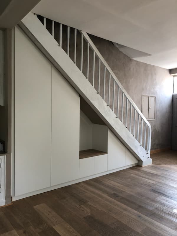 Vue d’angle du meuble sous escalier sur mesure, dressings blancs et niche d’accueil avec banc