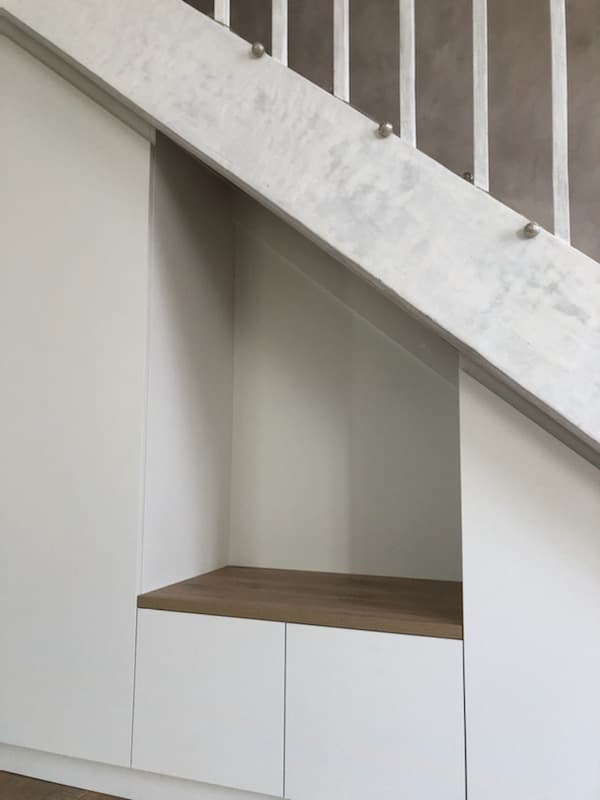 Détail de la niche d’accueil sous l’escalier : banc en chêne clair et rangements bas blancs pour les chaussures