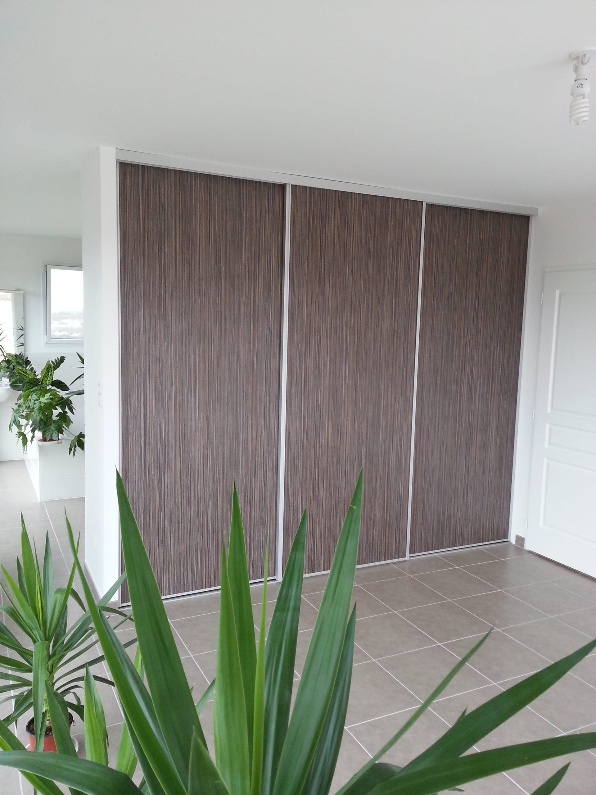 Placard coulissant trois vantaux aspect bois et profils aluminium blanc dans une entrée