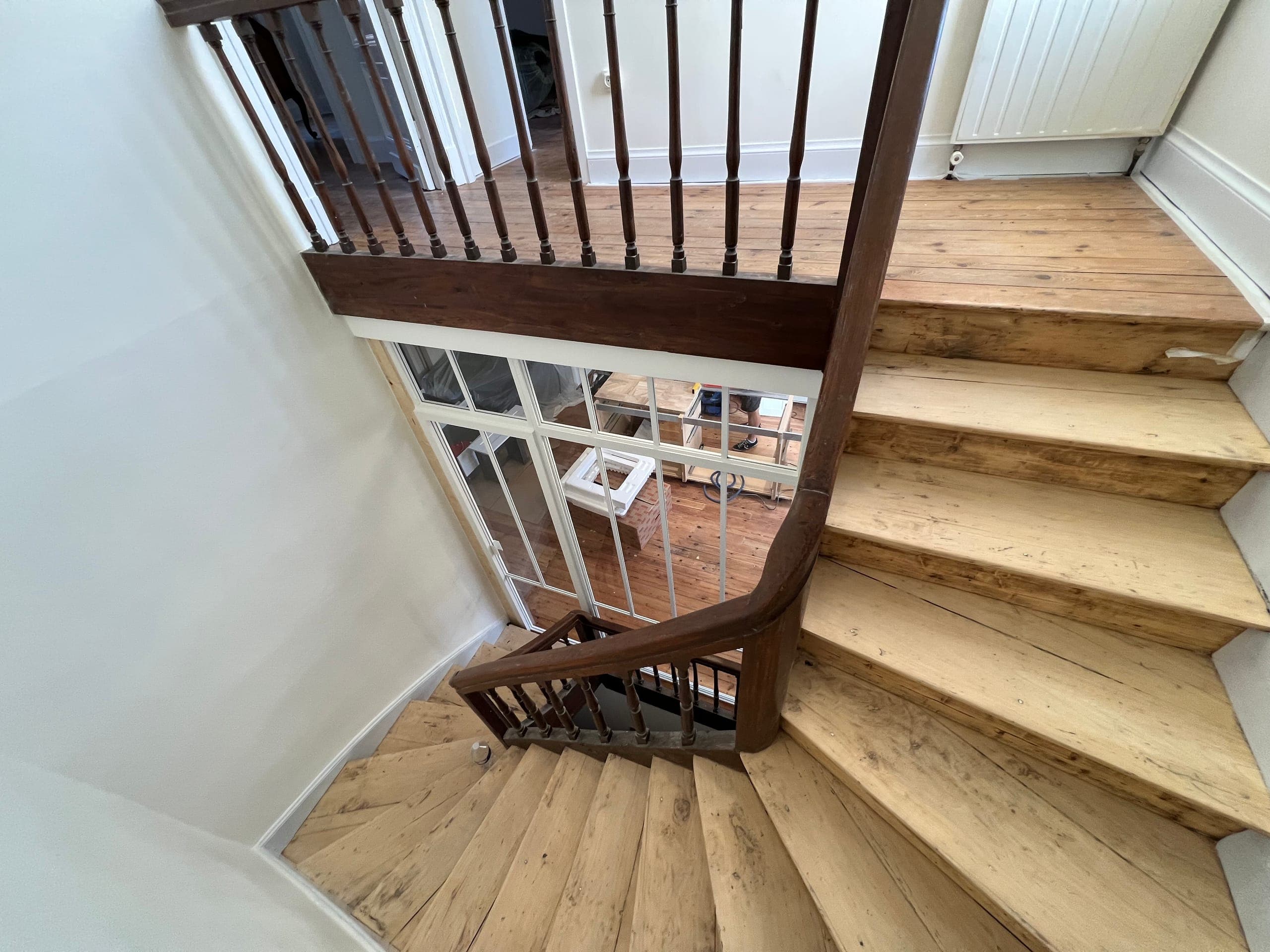 Vue plongeante depuis l’escalier en bois vers la verrière blanche, lumière naturelle circulant entre les niveaux