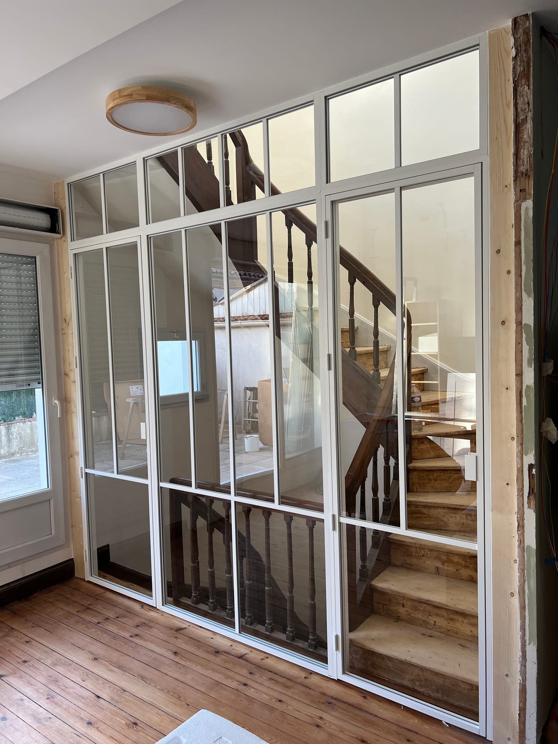 Verrière intérieure toute hauteur en aluminium blanc et verre transparent séparant deux niveaux dans une maison de ville à Agen